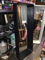 Front and angled side view of large black framed mirror showing size and minor scuffs on frame.