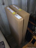 Two vertical unopened cardboard boxes labeled with IKEA Hauga stickers in a dimly lit storage area.