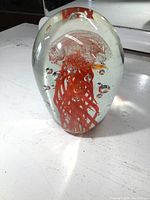 Side view of the clear glass paperweight showing the red jellyfish design inside, placed on a white surface.