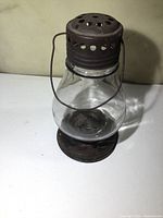 Front and side view of an antique skaters style lamp showing clear glass globe, metal base and perforated metal top with ventilation holes