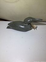 Front side view of the soapstone loon sculpture on a flat white surface showing the detailed carved and etched feather design.