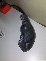 Three angled views of vintage soapstone seal sculpture showing polished black stone with white carved detail around eyes and head, curved flippers, and smooth rounded body form. Signed on bottom and original price tag attached.