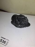 Side angle of dark soapstone sculpture showing polar bear holding a human figure in its mouth on a smooth base.