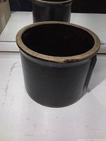 Front and side view of antique stoneware crock showing the dark glossy glaze and unglazed rim.