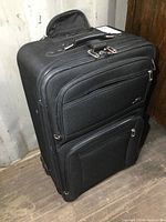 Front view of a 27" black suitcase showing two zippered outer pockets with the top handle visible.