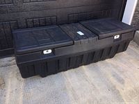 Front view of the large black heavy-duty resin truck toolbox placed on concrete, showing two locking compartments with metal latches and textured lid surface.