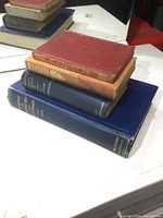 Photo showing stack of four vintage hardcover books of varying colors and sizes.