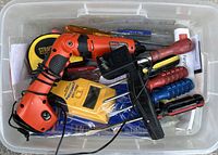 Top view of plastic bin filled with assorted vintage tools including electric drill, screwdrivers, and measuring tools.