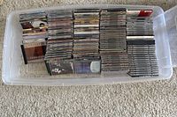 Plastic bin containing approximately 132 assorted music CDs stacked vertically, showing variety of cover art.