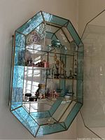 Full view of the glass wall display cabinet with textured blue-green glass border showing all figurines and decorative items inside.