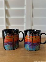 Front view of the Laurel Burch Rainbow Cat mug showing full cat design with orange, red, purple, and blue stripes, heart shapes above, and spiral patterns under the cat.