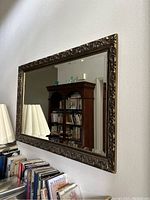 Angle view of vintage ornate carved floral wall mirror showing reflective quality and detailed carved pattern on frame.