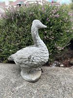 Front view of the vintage stone duck statue positioned outside with green bushes in the background.