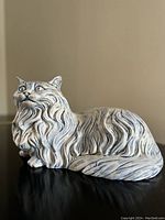 Front angled view of ceramic cat figurine showing detailed fur texture painted in white and blue, lying posture with alert expression.