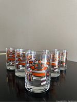 Five clear glasses with colorful striped cat designs in exercising poses lined up on a dark surface.