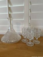 Side view of vintage crystal cut glass decanter with five matching wine glasses, showing diamond cut details on the glass surfaces.