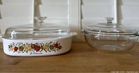 Two vintage Pyrex Corning bowls with and without Le Romarin pattern and matching lids on wooden surface