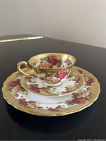 Photo showing the tea cup, saucer, and dessert plate stacked, displaying the golden rose floral design with gold rim.