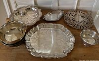 All seven silver-tone serving trays and bowls arranged on wood surface, showing different shapes and sizes in the lot.