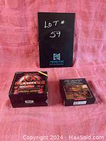 Photo showing two boxed CD sets on a pink fabric background, front view, one with the label '100 Rock & Roll Hits Happy Days Original Artists' and the other 'The Greatest Classical Collection'.