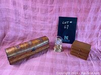 Lot photo showing Hermler clock under glass dome centered with two wooden trinket boxes on either side, against pink backdrop.
