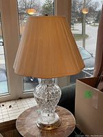Photo of the vintage crystal lamp with beige pleated fabric shade on a tiled side table in front of windows