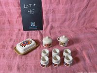 Full set of Esma dishes displayed on pink fabric backdrop showing butter dish, cream, sugar, and six egg cups with floral decoration.