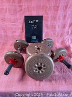 Photo showing the set of weights and bar arranged on a pink fabric background, with the lot number sign behind them.