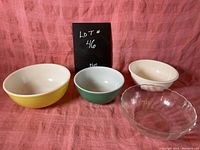 Set of four mid century modern mixing bowls including two Pyrex bowls, one plastic, and one glass, displayed on pink fabric.