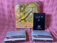 Wool blanket in original packaging with bold golden mustard color, two twin sheet sets in original packaging, all displayed on a pink background.