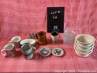 Photo showing full assortment of cups, bowls, mini decorative plates, glass bowls, pottery piece, and small metal shakers on pink cloth background.