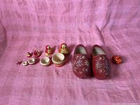 Nesting dolls separated into pieces and pair of red wooden clogs on pink fabric background
