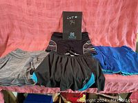 Four pieces of ladies activewear: two skorts and two shorts, displayed on a pink background.