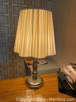Full view of the vintage silver tri-lite table lamp with pleated beige lampshade on a wood surface, background with geometric patterned wallpaper.