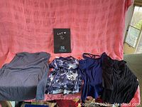 Four women's tank tops displayed against a pink backdrop including grey, floral, navy blue, and black tanks
