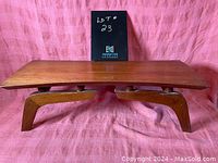 Front view of the teak bench showing the curved legs and flat seat.