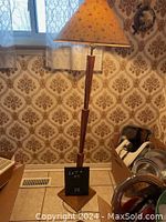 Full view of teak floor lamp with floral lampshade against vintage wallpaper.