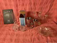 Full lot shot showing all items on red backdrop: shaker set (metal and box), 2 wine flutes, candelabra, sugar bowl, creamer, jigger, and serving bowl.