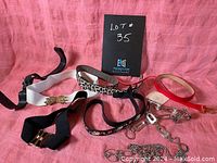 Photo of assortment of 7 vintage belts in various styles, colors and materials, laid on a pink fabric background.