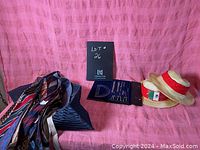 Photo showing vintage men's ties loosely laid on a chair, two Panama straw hats side by side, and vintage geometry set in navy blue folder on a pink background