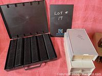Black plastic slide holder case open showing multiple vertical slots inside carrying case alongside grey slide storage box with two drawers and a black booklet.
