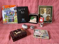 Full lot showing paint by numbers set, black writing paper pack, ceramic dishes, photo frame, wooden box, and other small decorative items on pink background.