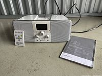 Boston micro stereo system with remote control and user guide booklet placed on a concrete floor in a metal storage unit.