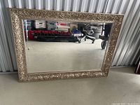 Full view of large rectangular mirror with ornate frame leaning against a storage unit wall.