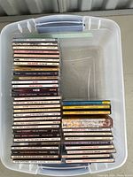 View of a clear plastic bin containing stacked country music CDs in jewel cases, showing spines with artist and album titles.