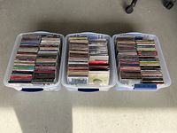 Three plastic storage bins filled with used rock CDs in jewel cases