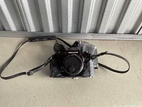 Front view of Nikon Nikkormat camera with lens and attached shoulder strap, inside worn camera case on concrete surface