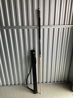 Full view of the pool cue and carrying case leaning against a corrugated metal backdrop, showing length and overall condition.