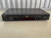 Front view of Sony DVD player showing full width and control buttons, disc tray, and display screen.