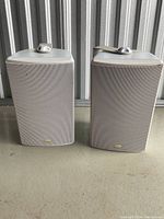 Two beige Klipsch outdoor speakers with metal mesh fronts and top mounting brackets, showing dust and signs of wear.